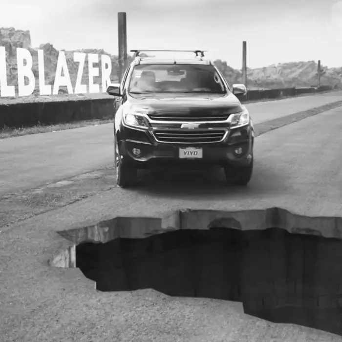 Una carretera larga y amplia con una camioneta marca Chevrolet estacionada al borde de una peligrosa ruptura gigante en la carretera